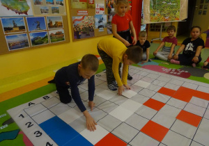 Troje dzieci stoi na macie do kowania, układają kolorowe płytki zgodnie z kodem, tworząc mapę Polski.
